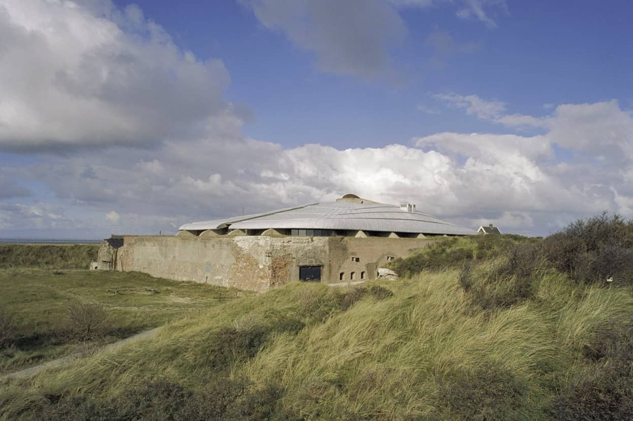 In het midden van de duinen staat een vierkant bakstenen gebouw met een rond laag puntdak.