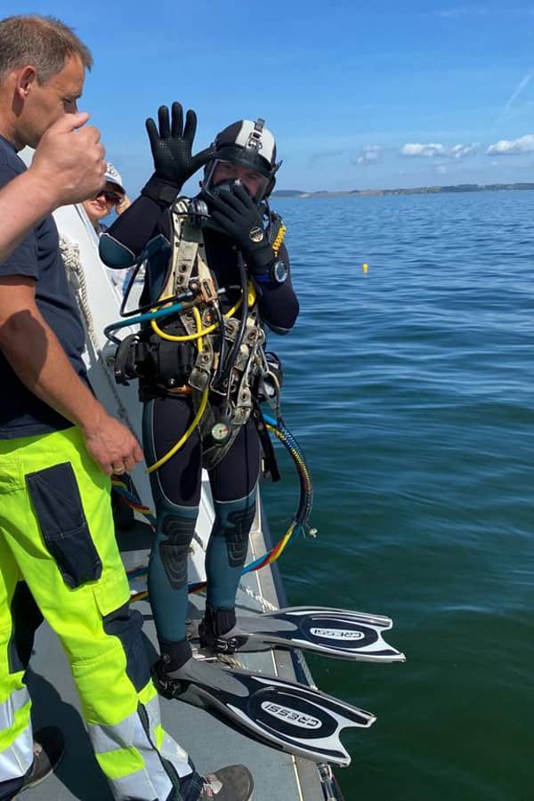 A diver stands on the gunwale of a boat ready to dive in