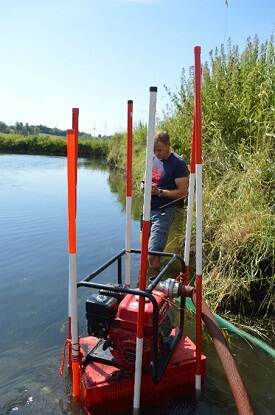 Man stands at dredging pump on the bank of a river