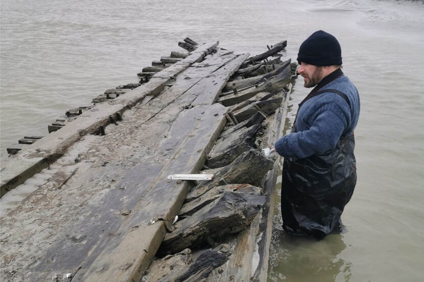 Man stands knee deep in the water near part of the shipwreck.